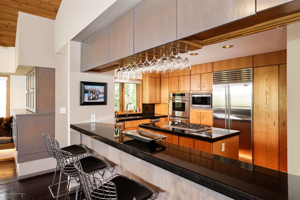 Modern kitchen with warm wood cabinets, stainless appliances, and a long black-counter breakfast bar.