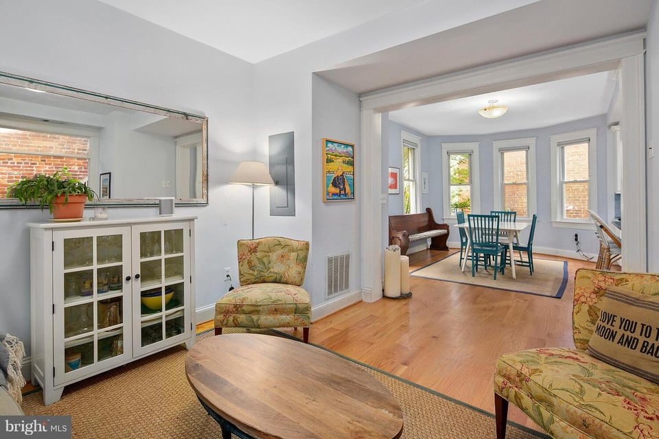 Living and dining room with hardwood floors, bay windows, and a teal dining set.