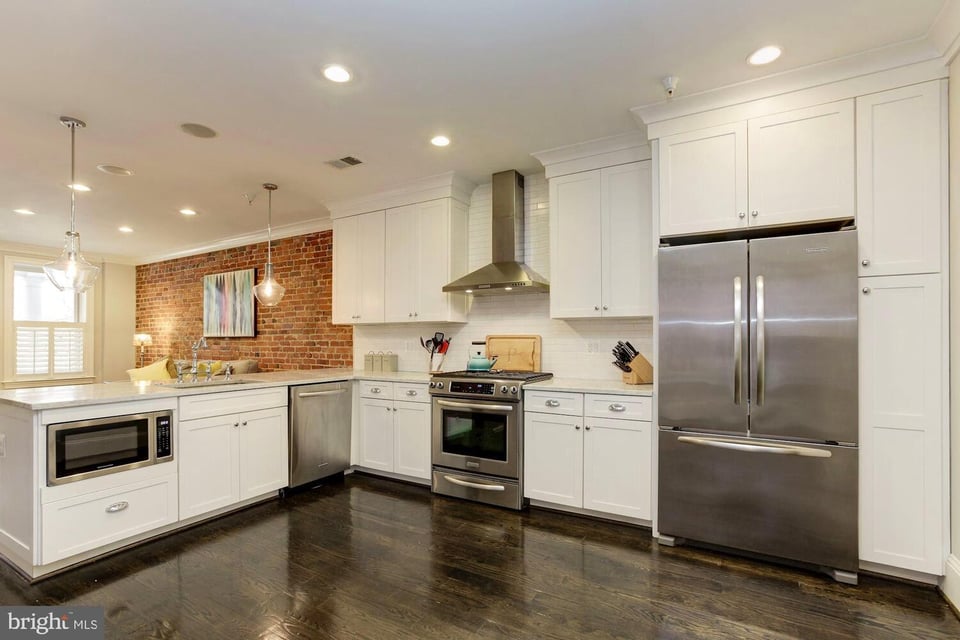 Kitchen with white cabinetry, stainless steel appliances, and a red brick accent wall.