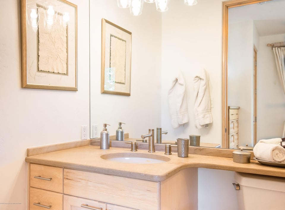Bathroom vanity with a pale stone counter, inset sink, and light wood cabinetry.