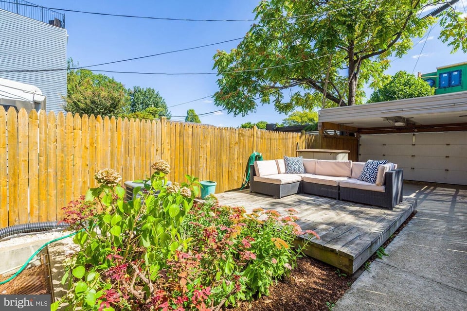 Backyard patio with a raised deck, sectional seating, and flowering garden beds.