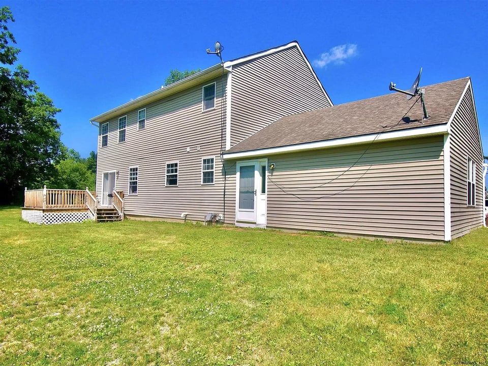 Rear exterior of a two-story home with a wooden deck and broad grassy lawn.