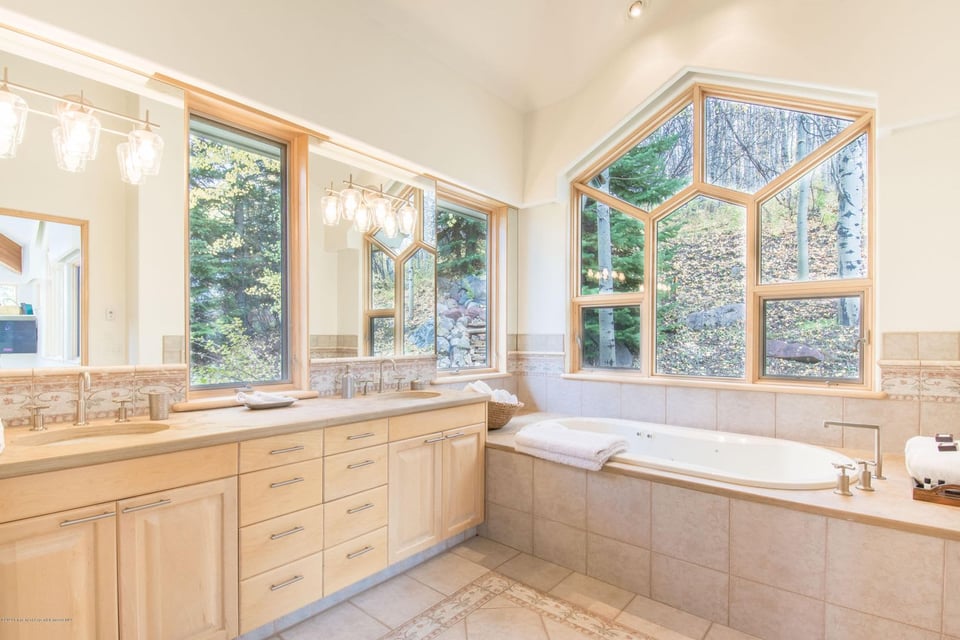 Bathroom with a long wood vanity, soaking tub, and large windows overlooking trees.