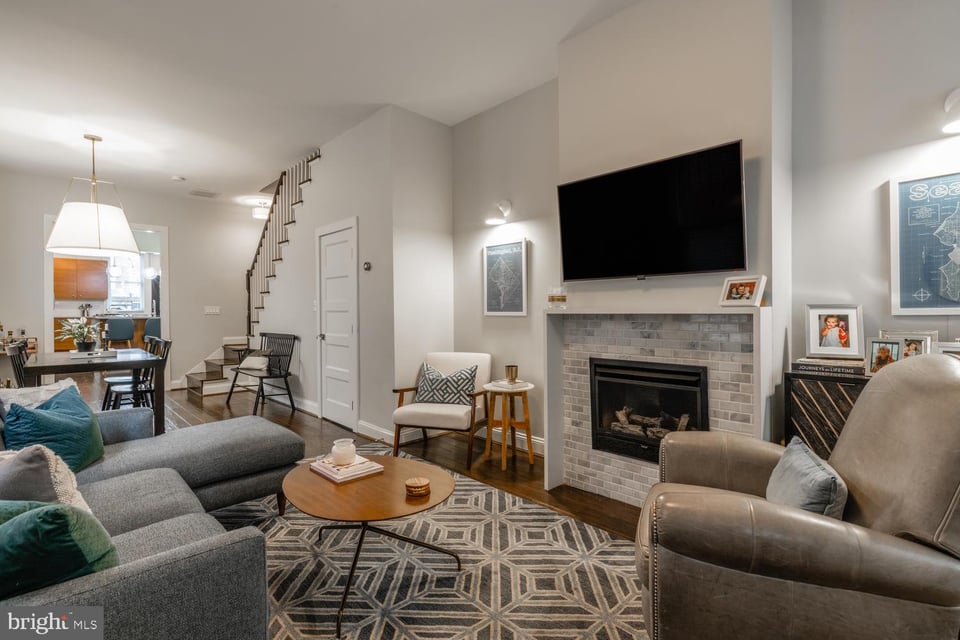 Living room with a gray sectional, geometric rug, tiled fireplace, and television above the mantel.