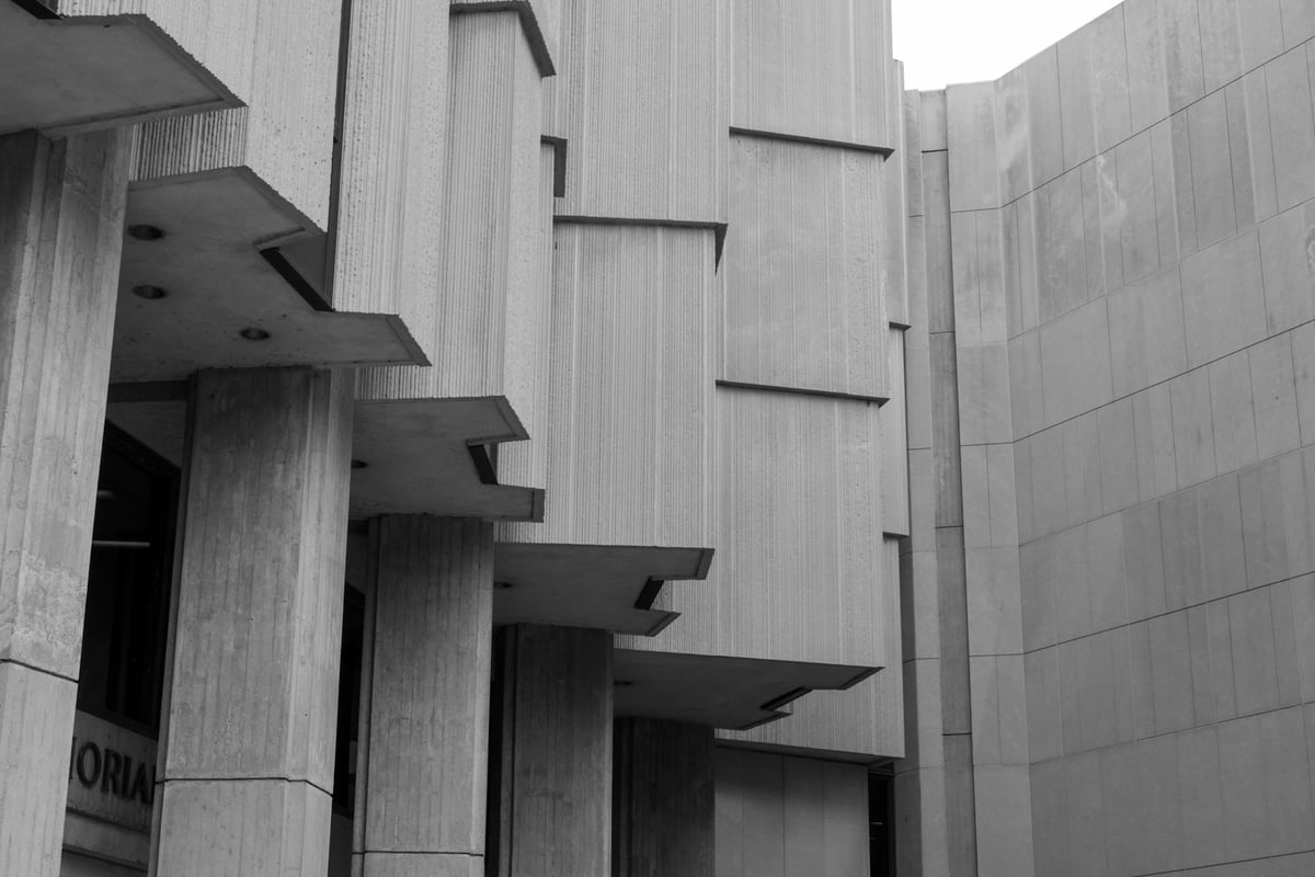 Modern concrete building facade with ribbed panels, projecting ledges, and massive columns.