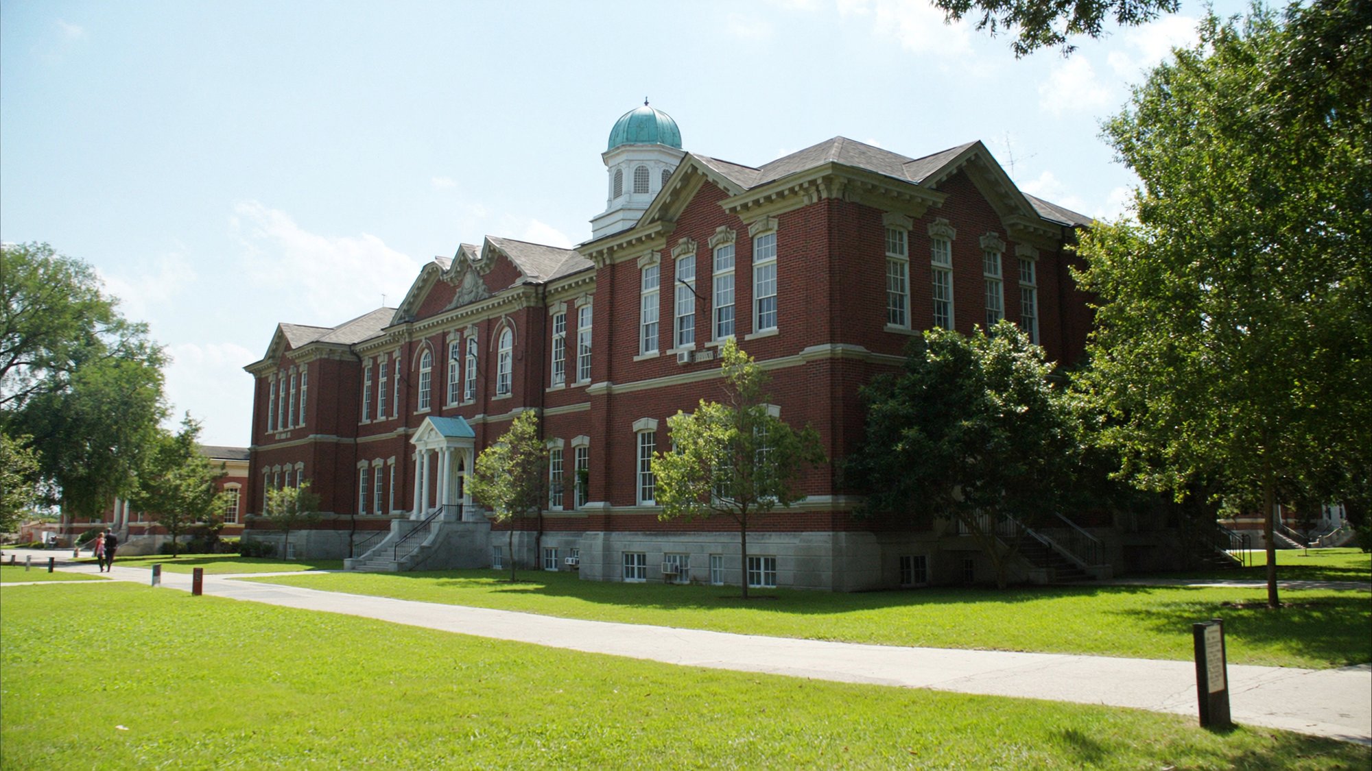 A classic red brick school building on a green lawn under a bright sky