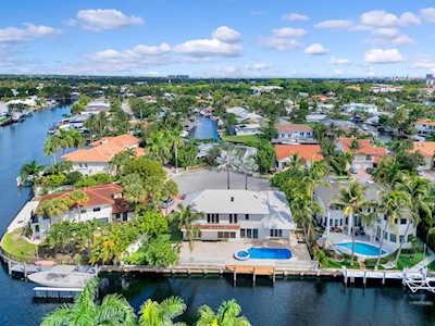 Waterfront home with a gray roof and blue pool beside a palm-lined canal.