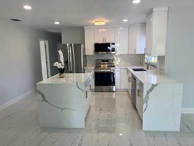Modern white kitchen with a large stone island, stainless steel appliances, and glossy marble-look floors.