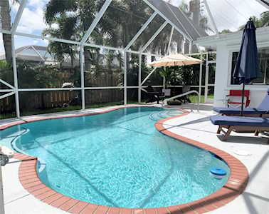 Backyard pool in a screened enclosure with curved brick coping and lounge chairs.