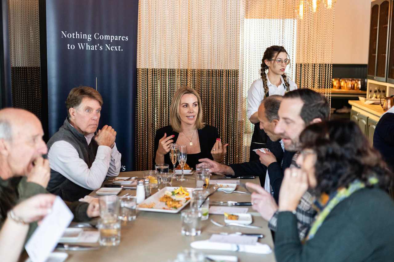 Real estate professionals gather around a table beneath a “Nothing Compares to What’s Next” banner.