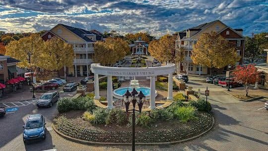 Smyrna Market Village’s central fountain and landscaped roundabout, surrounded by autumn trees and multi-story buildings.