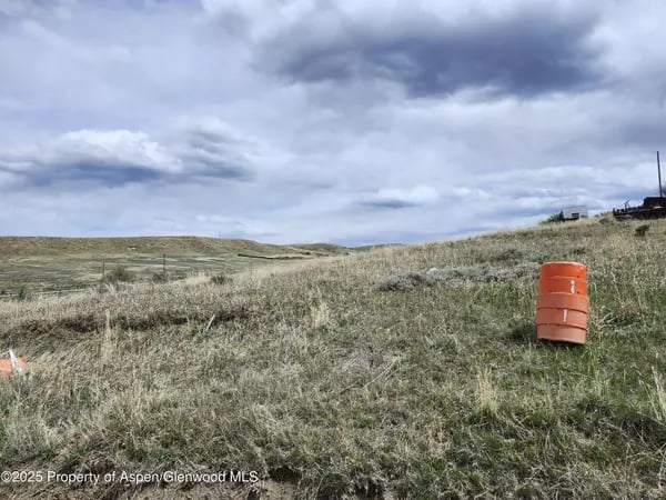 Vacant grassy hillside with an orange barrel in the foreground and distant structures on the ridge.