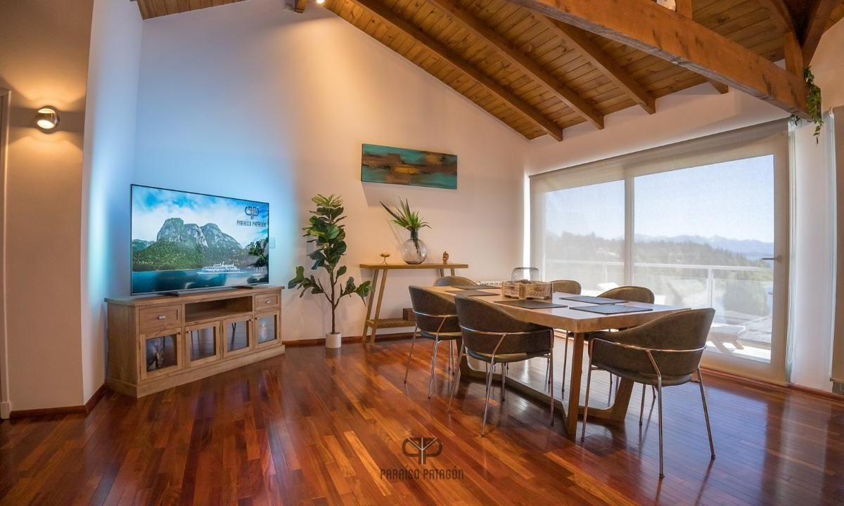 Dining area with a vaulted timber ceiling, polished wood floors, and mountain views through glass doors.