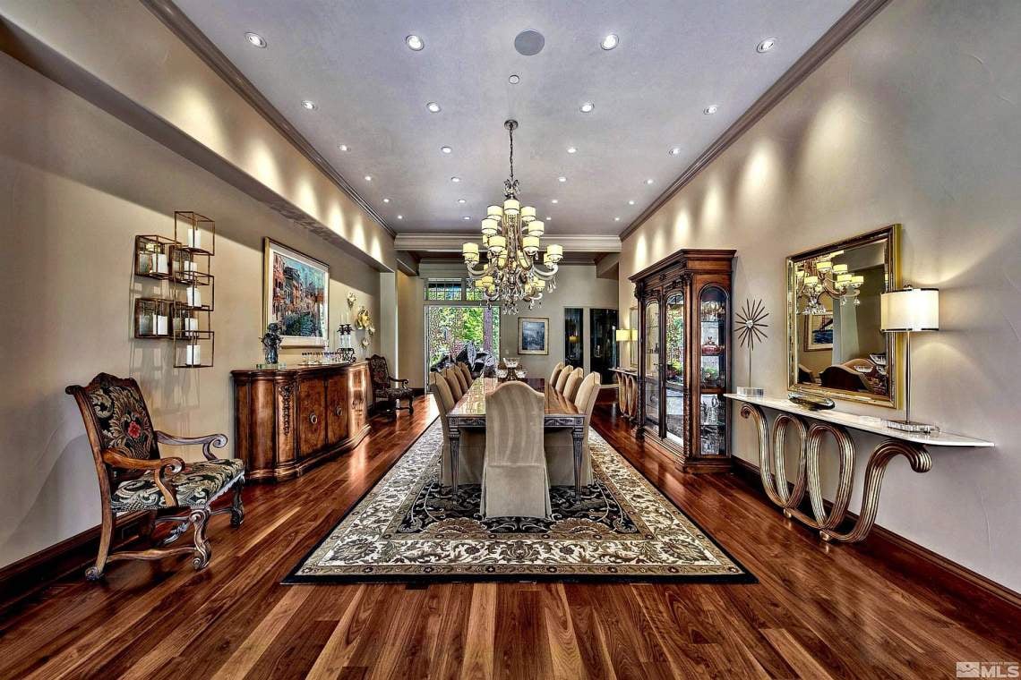 Formal dining room with a chandelier, polished hardwood floors, and a long table on a patterned rug.