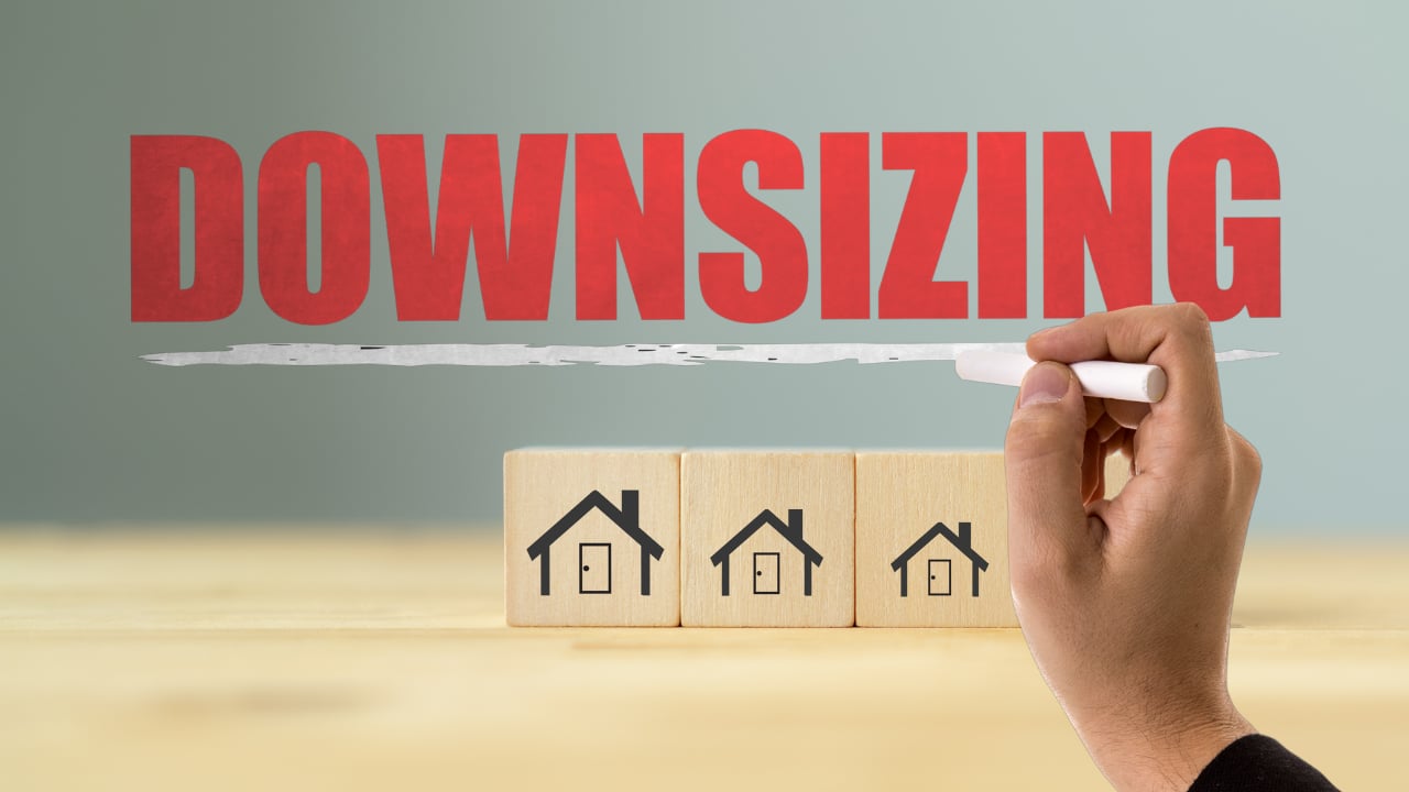 Downsizing illustrated with three wooden house blocks and a hand underlining the word “DOWNSIZING.”