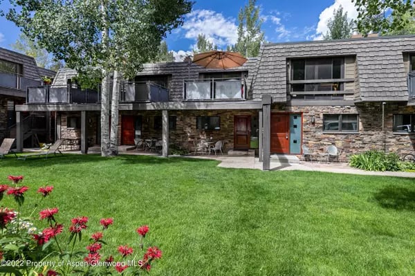 Two-story residence with stone walls, red doors, and a broad lawn.