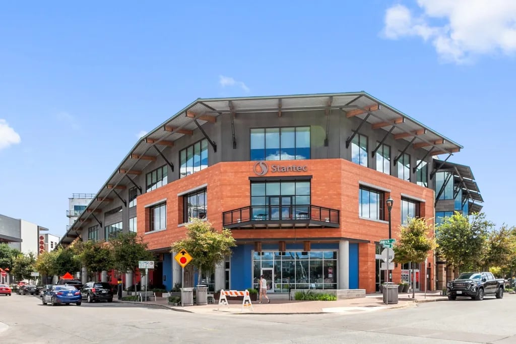 Modern corner commercial building with orange-red brick, a blue storefront, and a broad metal roof.