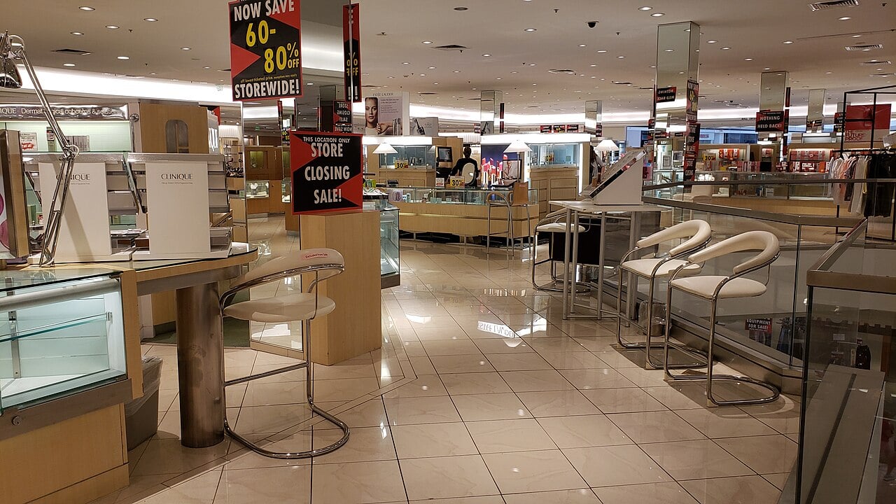 Department store cosmetics floor with closing-sale signs, display counters, and empty seating.