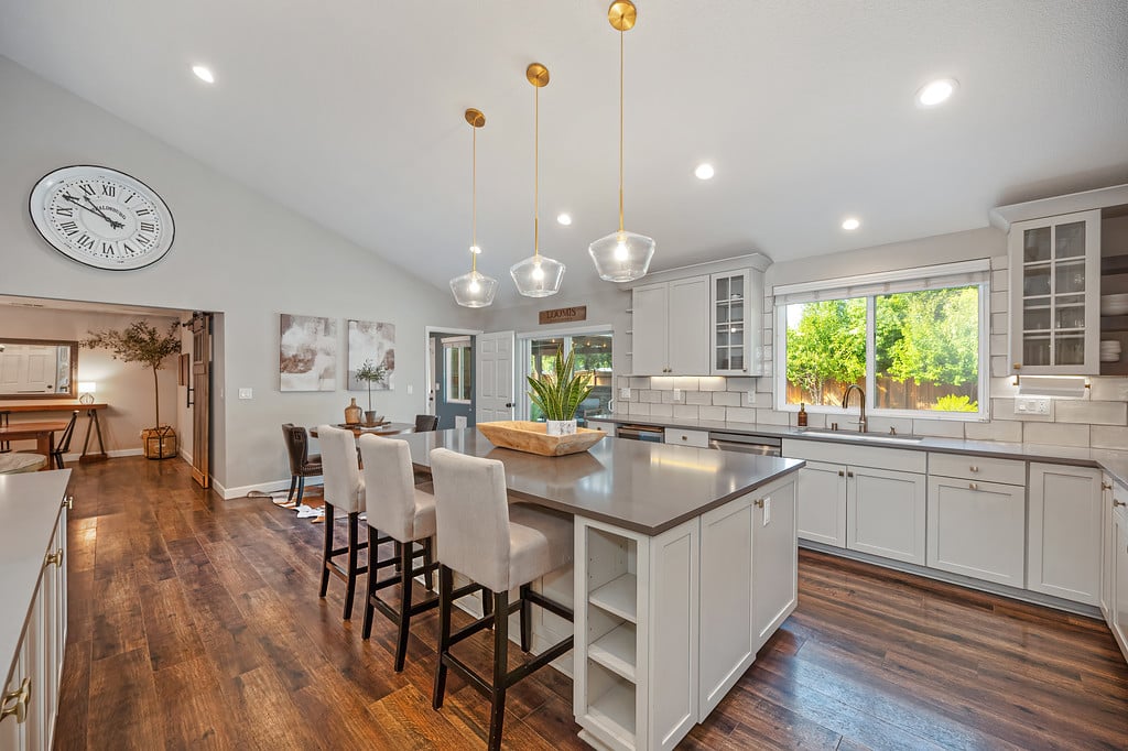 Bright kitchen with a large island, white cabinetry, pendant lights, and dark wood floors.