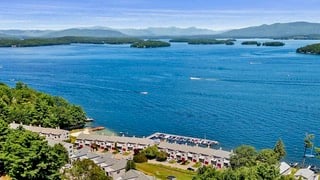 Aerial view of a blue lake and waterfront homes, with wooded islands and distant mountains.