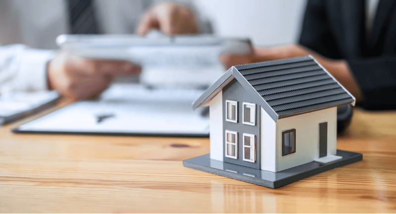 A model house on a desk beside paperwork being reviewed.