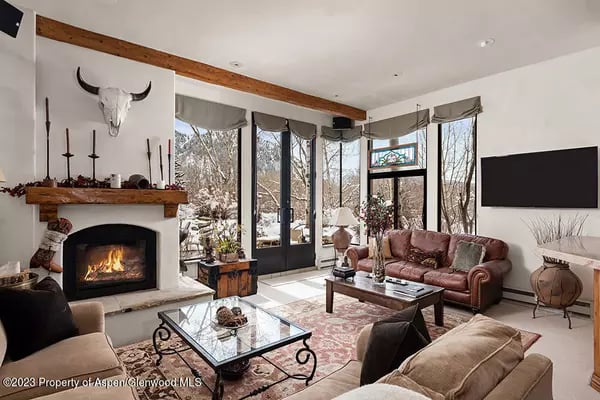 Living room with a stone fireplace, leather seating, and tall windows overlooking a snowy landscape.