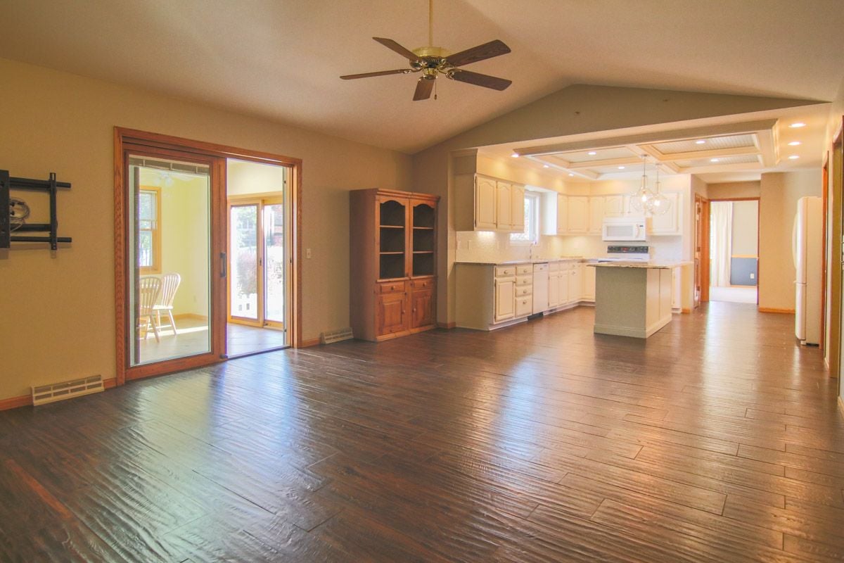 Open kitchen with cream cabinets and island beside sliding glass doors and dark wood flooring.
