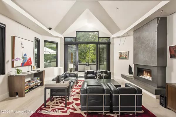 Living room with vaulted ceilings, black-framed windows, contemporary furnishings, and a fireplace.