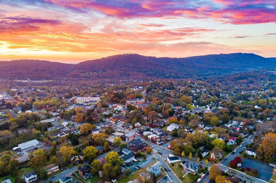 Aerial view of a town beneath wooded hills and a vivid sunset sky.