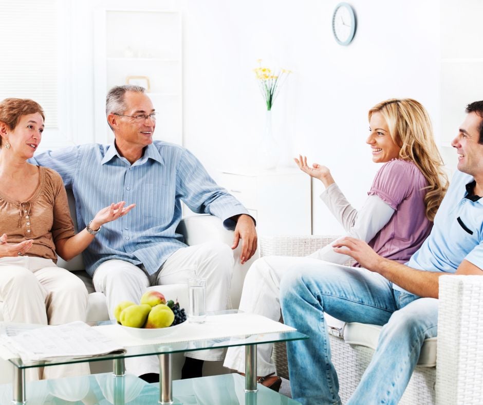 An older couple talks with a younger couple in a bright living room.