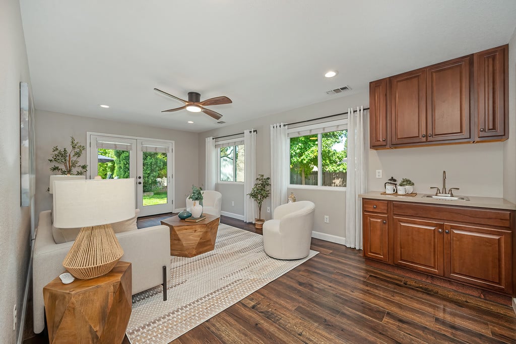 Living room with white seating, wood floors, and a kitchenette beside doors opening to the garden.