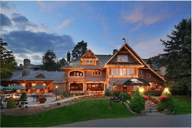 Mountain resort exterior glowing with warm lights beside a landscaped garden and outdoor dining patio.
