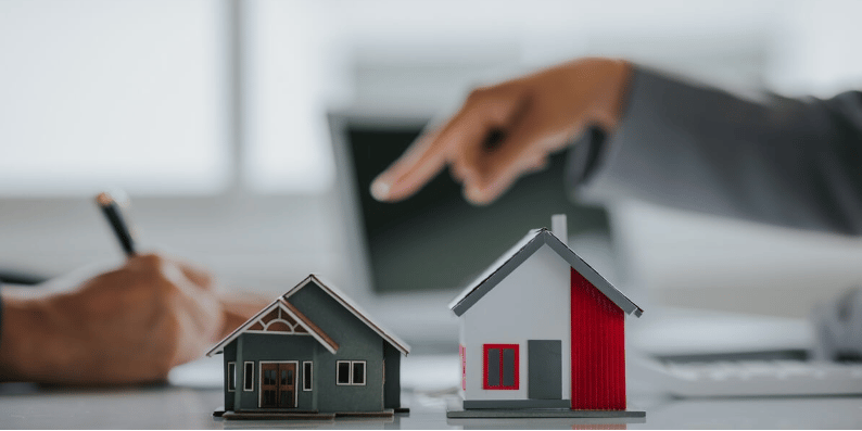Hands discuss two model houses, one dark and one white with red siding.
