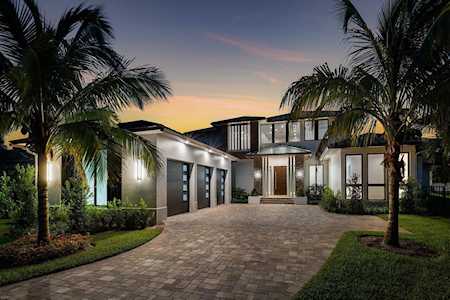 Modern two-story home with illuminated windows, a stone driveway, and palm trees at dusk.