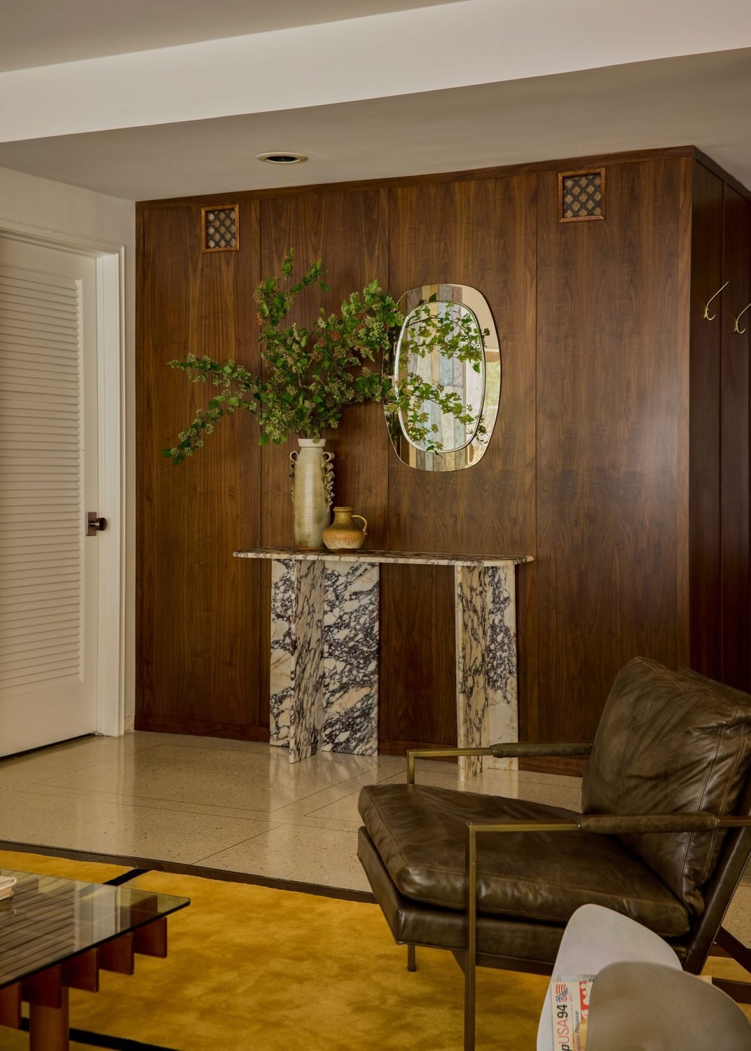 Entry hall with a walnut-paneled wall, an antique console, and a mirror.
