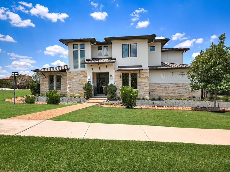 Modern two-story house with a stone facade, attached garage, and walkway across the lawn.