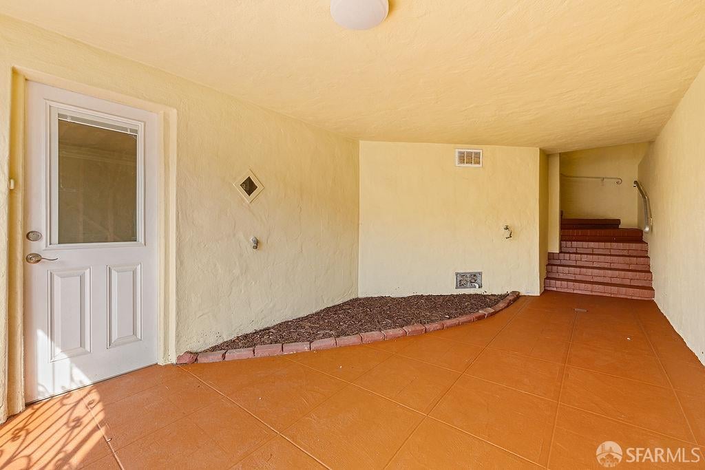 Covered entry with an orange-tiled floor, white door, narrow planting bed, and steps at the far end.