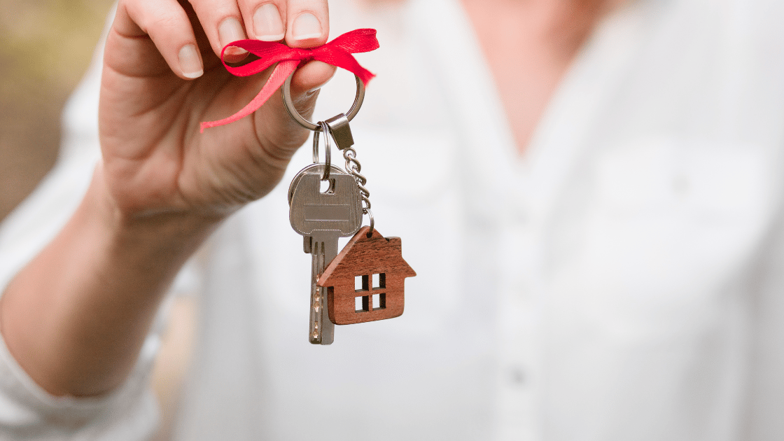 A person holding a house key with a red ribbon and wooden house keychain, symbolizing a stress-free new home purchase in Oregon
