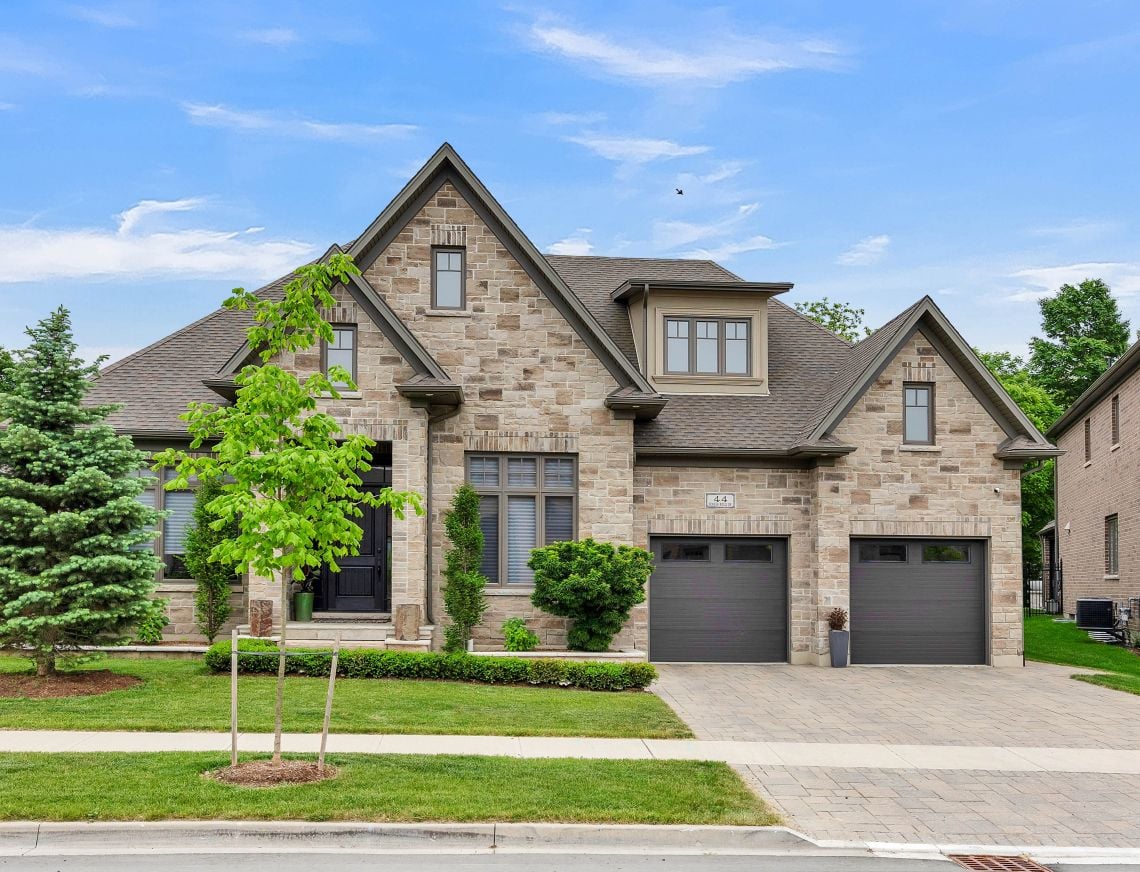 Stone-clad home with multiple gables, two garage doors, and a landscaped front lawn.