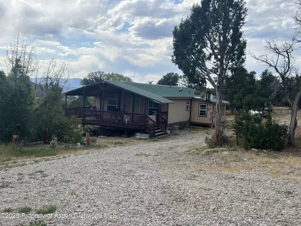 Single-story home with a covered porch beside a broad gravel driveway and mature trees.