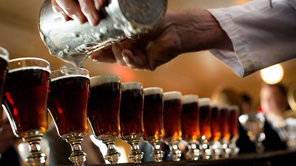 Barista pouring cream into row of Irish coffee glasses on tray