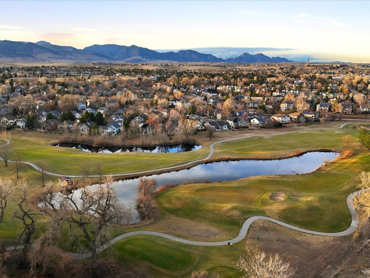 Aerial view of a Colorado residential neighborhood with golf course, ponds, and mountain views, illustrating local market conditions and home values.