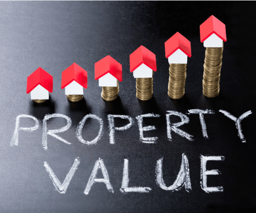 Miniature red-roofed houses rise on stacks of coins above the words “PROPERTY VALUE.”