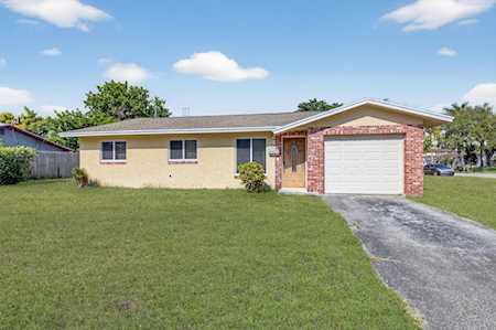 Single-story tan stucco house with a brick-accented garage, broad lawn, and paved driveway.