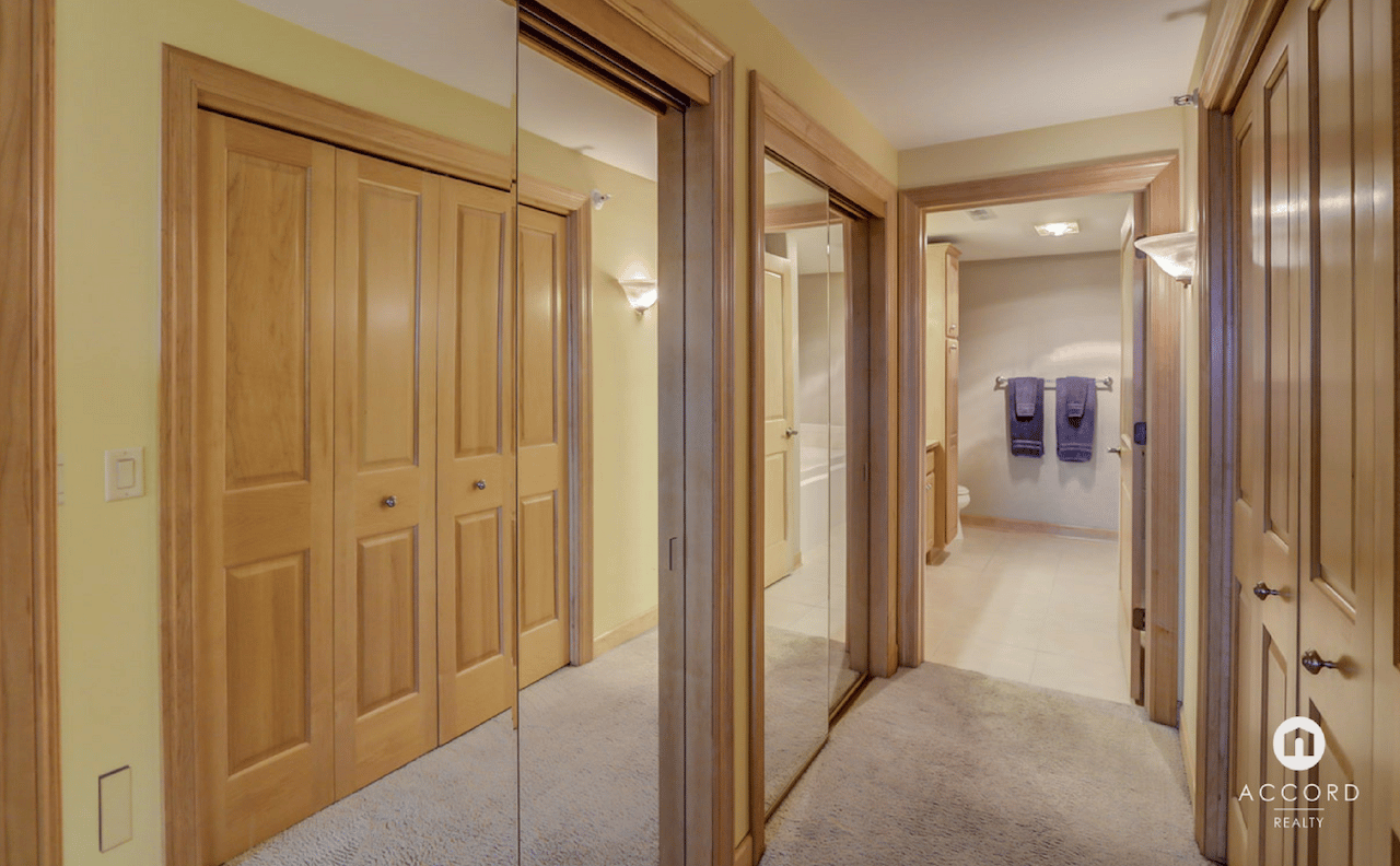 Condo hallway with mirrored closet doors and wood trim, opening to a tiled bathroom.