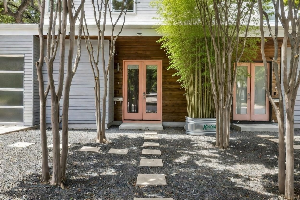 Front elevation of a modern duplex at 1302 S 5th St Unit A, Bouldin neighborhood, Austin, TX, designed by architect Steve Zagorski, with twin coral entry doors, cedar and white lap siding, and crepe myrtle trees.