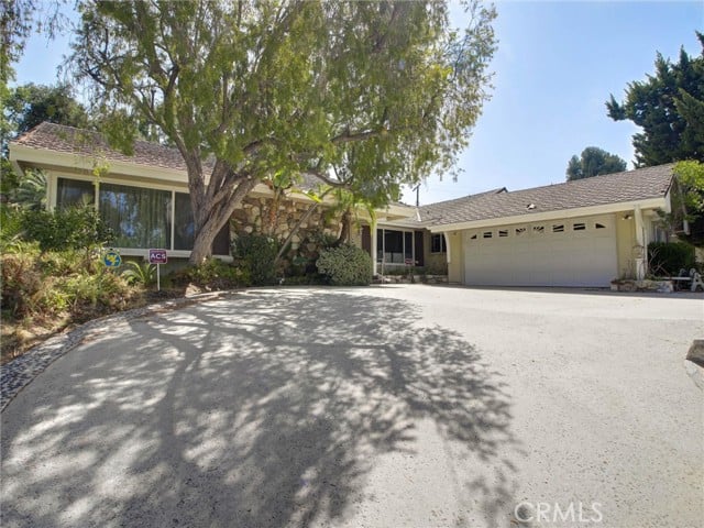 Single-story home with an attached garage and a broad, tree-shaded driveway.