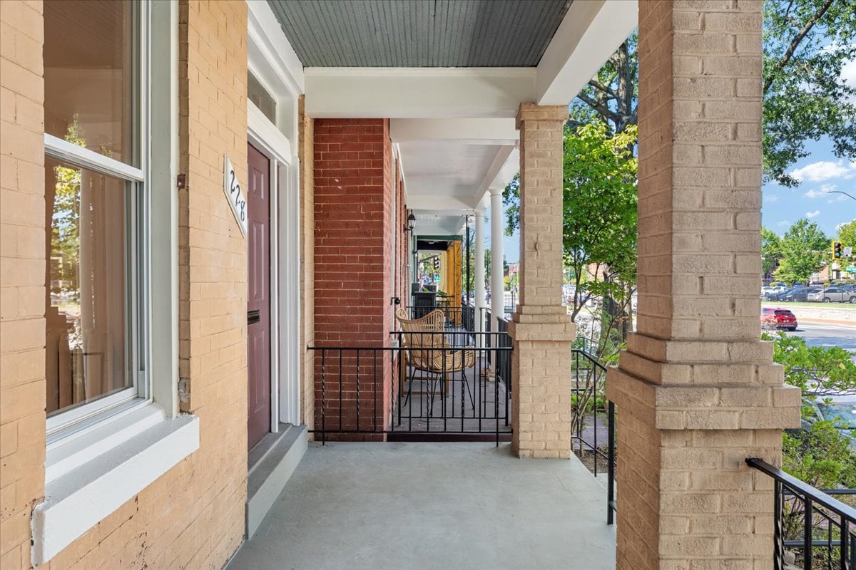 Covered brick front porch with a red door, black railing, and patio chairs.