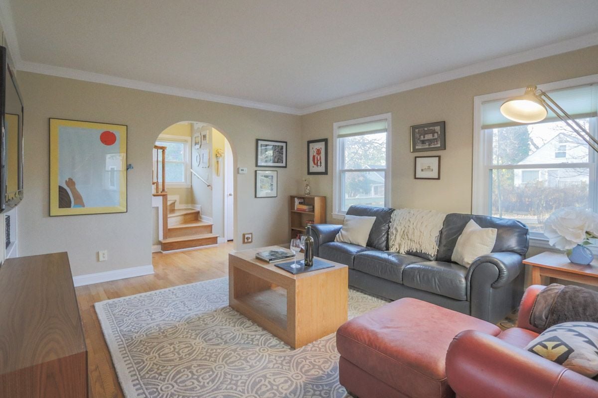 Furnished living room with a gray leather sofa, red armchairs, patterned rug, and arched doorway to a staircase.
