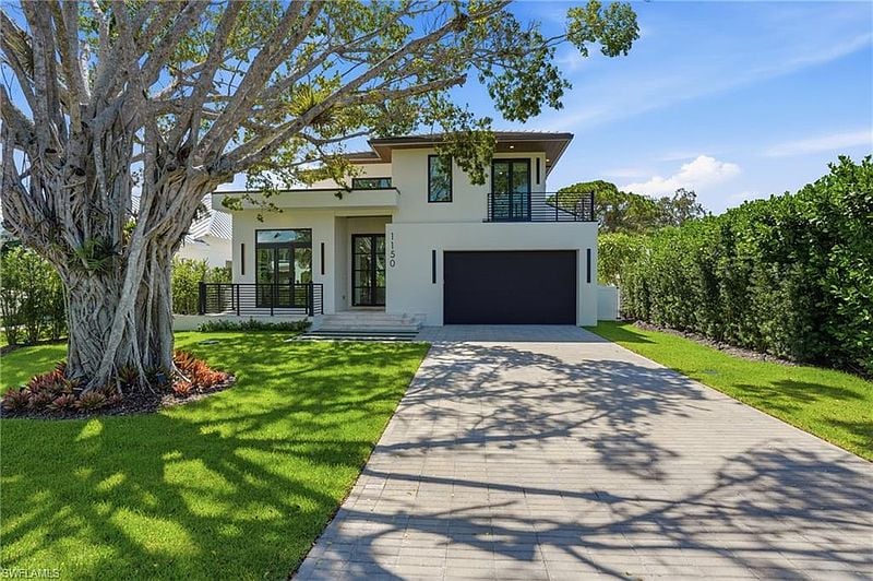 Modern white two-story home with a black garage, broad driveway, and large shade tree.